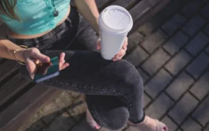 Customer holding a takeaway coffee and reading a text message on her smartphone