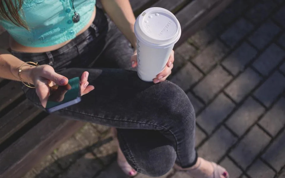 Customer holding a takeaway coffee and reading a text message on her smartphone