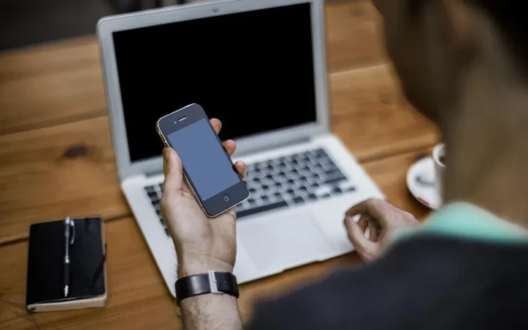 Business owner holding a smartphone in front of a laptop while replying to Google reviews