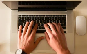 Hands typing review replies on a laptop keyboard at an office desk