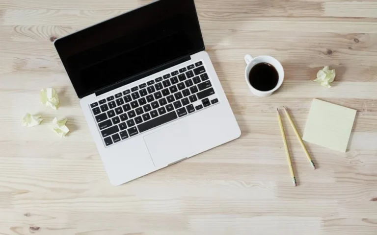 Laptop on a wooden desk with coffee and sticky notes, ready for writing customer emails